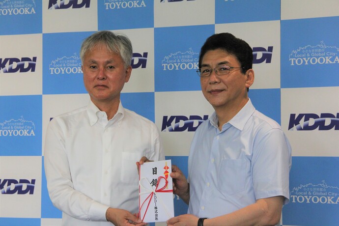 写真：KDDI株式会社理事関西総支社長の田中稔さんが関貫市長に寄付目録を手渡す
