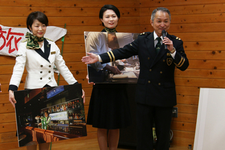 写真：バーカウンターの写真パネルを持つ女性と、説明する列車長長尾さん