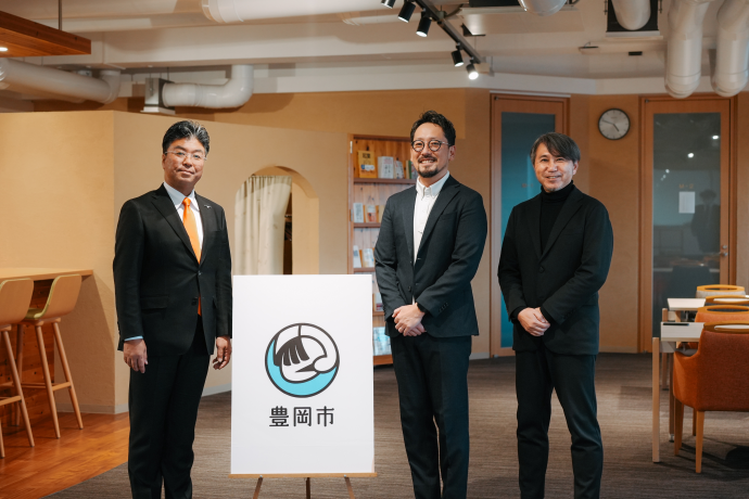 ロゴマークのパネルと一緒に写る門間市長、加賀さん、徳田さん