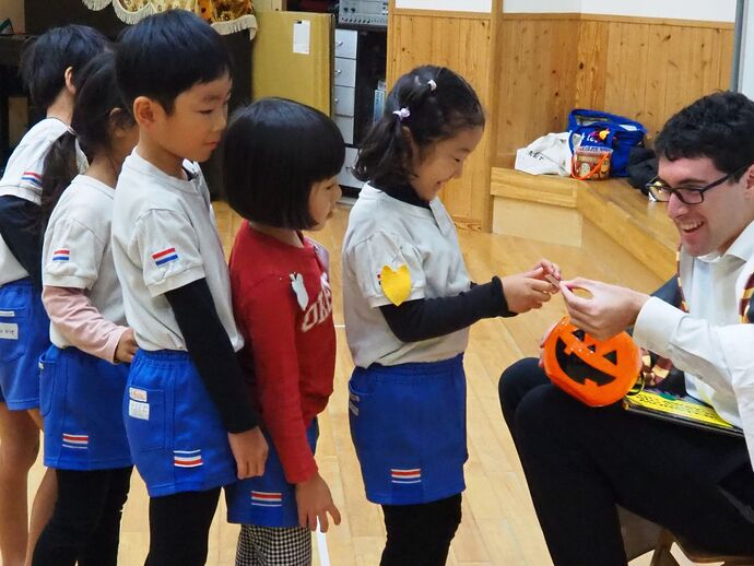 英語遊びの写真：“Trick or treat!”　ALTの先生にシールをもらう子ども