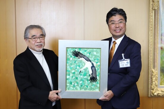 麦わら細工のコウノトリの作品を持つ神谷勝さん（左）と門間市長（右）の写真