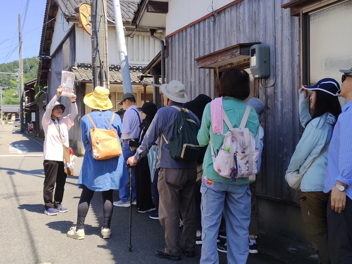写真を掲げながら参加者らに出石のまちなみを説明するガイド
